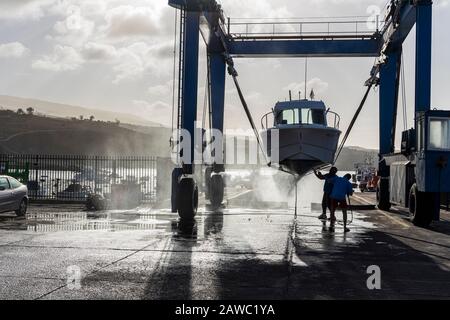 Nettoyage de la coque inférieure d'un bateau suspendu dans une grue de levage dans un quai sec au port de Playa San Juan, Tenerife, îles Canaries, Espagne Banque D'Images