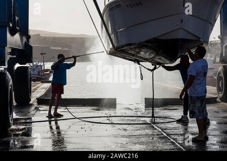 Nettoyage de la coque inférieure d'un bateau suspendu dans une grue de levage dans un quai sec au port de Playa San Juan, Tenerife, îles Canaries, Espagne Banque D'Images