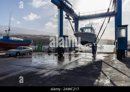 Nettoyage de la coque inférieure d'un bateau suspendu dans une grue de levage dans un quai sec au port de Playa San Juan, Tenerife, îles Canaries, Espagne Banque D'Images