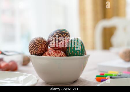 La cire colorée a peint des œufs de Pâques dans un bol sur une table en bois, des ornements peints en cire, des fleurs arc-en-ciel, des points Banque D'Images