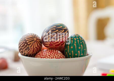 La cire colorée a peint des œufs de Pâques dans un bol sur une table en bois, des ornements peints en cire, des fleurs arc-en-ciel, des points Banque D'Images