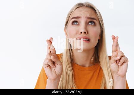 Gros plan Femme blanche blanche blonde, inquiète et très nerveuse, dans un t-shirt orange, les doigts croisés espoir dieu entend les prières comme sourcils de raie intense, anxieusement Banque D'Images