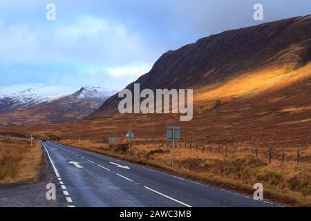 Route vide traversant l'Ecosse, avec des montagnes enneigées en arrière-plan. Banque D'Images