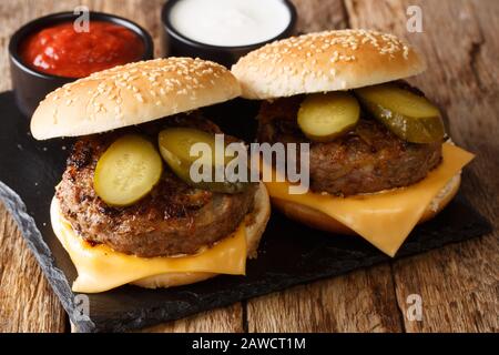 Recette traditionnelle de l'Oklahoma. Hamburgers à l'oignon frits avec fromage cheddar et cornichons sur une planche en ardoise sur une table. Horizontale Banque D'Images