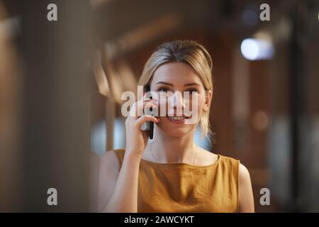 Portrait de la jeune femme avec des cheveux blonds souriant à l'appareil photo alors qu'il a une conversation sur le téléphone mobile Banque D'Images