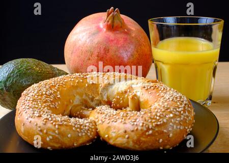Bretzel, gâteau sucré au thé, marmelade, avocat, tomates, grenade et verre de jus d'orange, disposés symétriquement sur une table en bois Banque D'Images