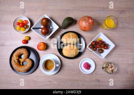 Bretzel, gâteau sucré au thé, marmelade, avocat, tomates, grenade et verre de jus d'orange, disposés symétriquement sur une table en bois sur blanc et Banque D'Images