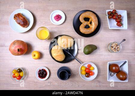 Bretzel, gâteau sucré au thé, marmelade, avocat, tomates, grenade et verre de jus d'orange, disposés symétriquement sur une table en bois sur blanc et Banque D'Images