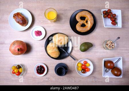 Bretzel, gâteau sucré au thé, marmelade, avocat, tomates, grenade et verre de jus d'orange, disposés symétriquement sur une table en bois sur blanc et Banque D'Images
