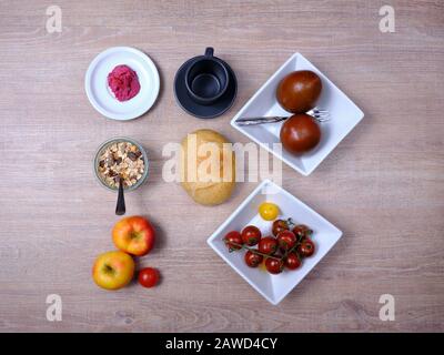 Bretzel, gâteau sucré au thé, marmelade, avocat, tomates, grenade et verre de jus d'orange, disposés symétriquement sur une table en bois sur blanc et Banque D'Images