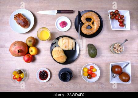 Bretzel, gâteau sucré au thé, marmelade, avocat, tomates, grenade et verre de jus d'orange, disposés symétriquement sur une table en bois sur blanc et Banque D'Images