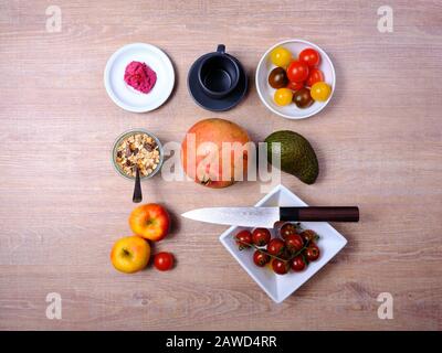 Bretzel, gâteau sucré au thé, marmelade, avocat, tomates, grenade et verre de jus d'orange, disposés symétriquement sur une table en bois sur blanc et Banque D'Images