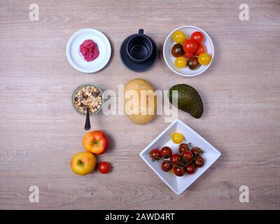 Bretzel, gâteau sucré au thé, marmelade, avocat, tomates, grenade et verre de jus d'orange, disposés symétriquement sur une table en bois sur blanc et Banque D'Images