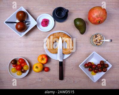 Bretzel, gâteau sucré au thé, marmelade, avocat, tomates, grenade et verre de jus d'orange, disposés symétriquement sur une table en bois sur blanc et Banque D'Images