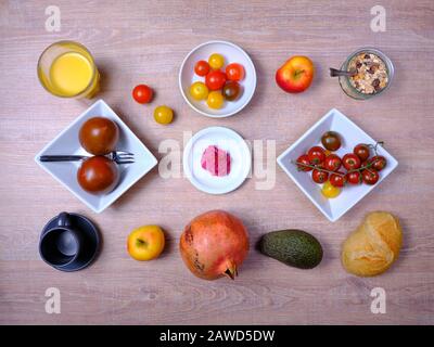 Bretzel, gâteau sucré au thé, marmelade, avocat, tomates, grenade et verre de jus d'orange, disposés symétriquement sur une table en bois sur blanc et Banque D'Images