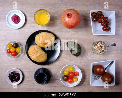 Bretzel, gâteau sucré au thé, marmelade, avocat, tomates, grenade et verre de jus d'orange, disposés symétriquement sur une table en bois sur blanc et Banque D'Images