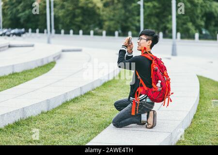 Moscou, Russie - 7 juillet 2017. Un jeune homme asiatique heureux avec un sac à dos lumineux sur ses épaules photographie le monument. Vue latérale Banque D'Images