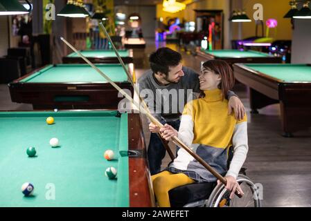 Belle fille handicapé dans un fauteuil roulant jouant au billard avec son petit ami Banque D'Images