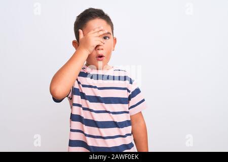 Beau garçon porté décontracté t-shirt rayé debout sur fond blanc isolé peeking dans le visage et les yeux de revêtement de choc avec la main, regardant th Banque D'Images