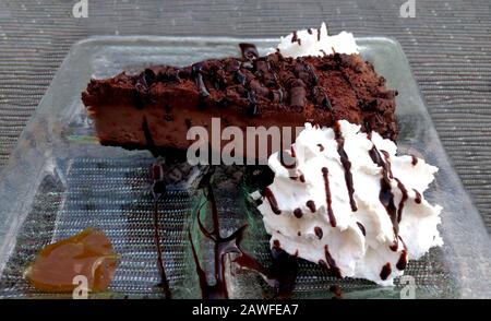 Une riche tranche de gâteau au fromage au chocolat noir, décorée de rubans de sauce au chocolat, et garnie de caramel et de crème fouettée Banque D'Images