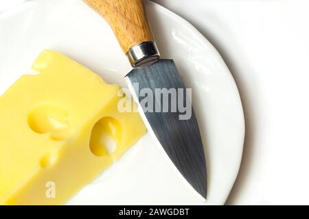 Fromage avec un couteau à fromage sur une plaque blanche. Morceau de fromage avec trous Banque D'Images
