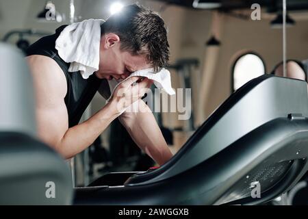 Un sportif qui évacue la transpiration de son front après avoir fait du jogging sur le moulin à filon dans la salle de gym Banque D'Images