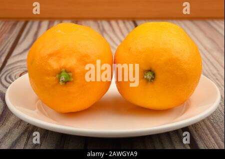 Deux citrons jaunes mûrs sur une plaque blanche sur fond en bois. Gros plan Banque D'Images