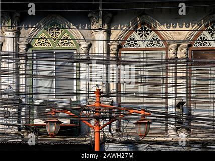 bangkok, thaïlande - 2020.02.04: une lanterne de rue, des lignes électriques et des câbles téléphoniques en face d'un immeuble historique de bureaux sur thanon song wat en chinat Banque D'Images