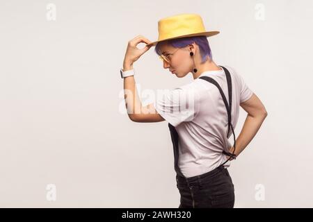 Portrait vue latérale d'une élégante fille hipster avec des cheveux violets et dans des salopettes portant un chapeau sur la tête, en regardant un espace vide pour votre publicité Banque D'Images