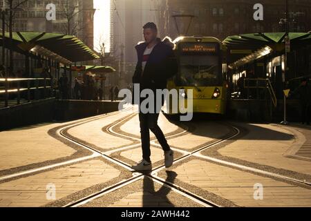 Un homme traverse la voie de la rue à l'arrêt de tramway Metrolink St Peter's Square Manchester avec un tramway jaune en arrière-plan. Banque D'Images