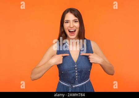 WOW, regarde-moi! Enchantée femme brunette émerveillez-vous dans une robe denim qui se montre impressionnée par une expression stupéfiée, qui se sent surprise et fière de suce Banque D'Images