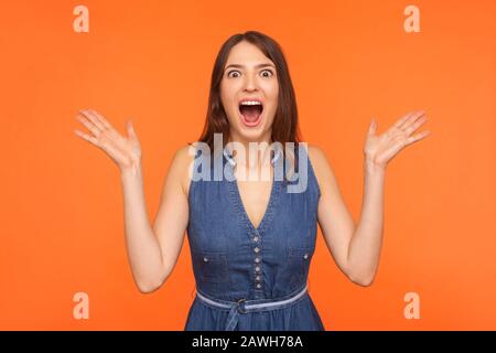 Choqué, la femme brunette impressionnée dans une tenue denim debout avec une large bouche ouverte et se levant les mains de surprise, regardant surmontée de l'appareil photo. Indoo Banque D'Images