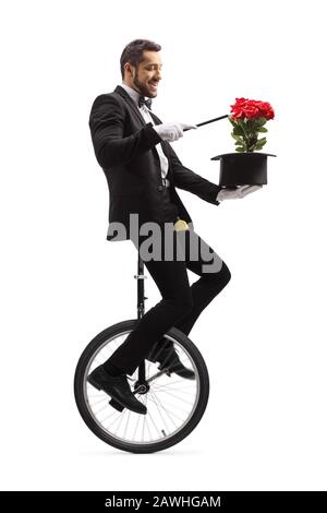 Magicien exécutant sur un unicycle avec une baguette magique, chapeau et roses rouges isolés sur fond blanc Banque D'Images