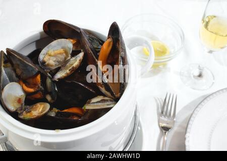 Pot de moules et de palourdes sur une table isolée contre une nappe blanche dans un restaurant Banque D'Images