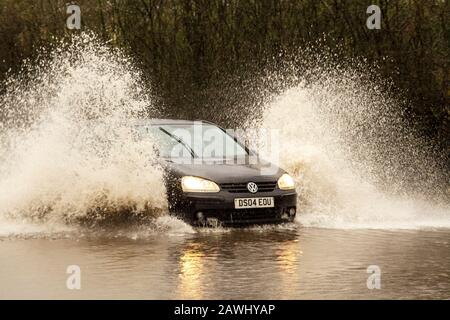 Une voiture qui traverse des eaux profondes et qui lance rapidement des jets d'eau sur une route à Kirkham, dans le Lancashire, au Royaume-Uni.Fév. 2020.Météo au Royaume-Uni ; les routes de la tempête Ciara ont été inondées à Kirkham.Crédit : MediaWorldImages/Alamy Live News Banque D'Images