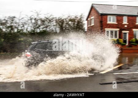 Une voiture qui traverse des eaux profondes et qui lance rapidement des jets d'eau sur une route à Kirkham, dans le Lancashire, au Royaume-Uni.Fév. 2020.Météo au Royaume-Uni ; les routes de la tempête Ciara ont été inondées à Kirkham.Crédit : MediaWorldImages/Alamy Live News Banque D'Images