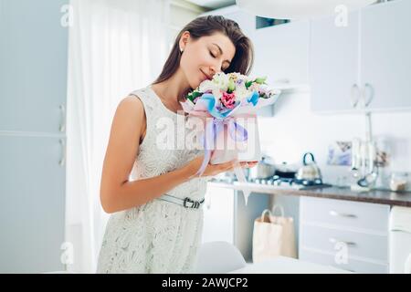 Saint Valentin, journée des femmes. La femme sent le bouquet de fleurs dans une boîte cadeau sur la cuisine. Surprise. Présent pour les vacances Banque D'Images