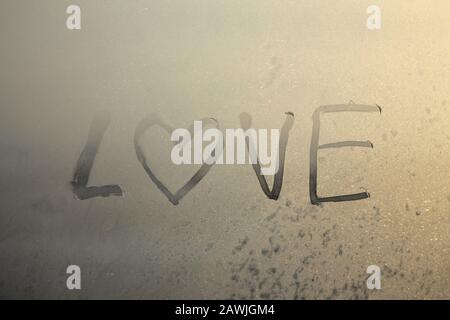 Mot amour écrit sur une fenêtre gelée. Concept amour Saint-Valentin. Texture d'arrière-plan brillante, motif. Fond en verre gelé. Banque D'Images