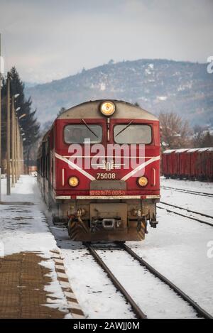 Gare de Velingrad, Bulgarie - 8 février 2020: Train avec locomotive rouge et wagons verts arrive à la gare. Banque D'Images
