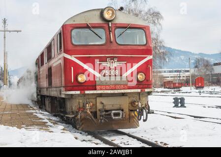Gare de Velingrad, Bulgarie - 8 février 2020: Train avec locomotive rouge et wagons verts arrive à la gare. Banque D'Images