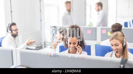 Travailleur de centre d'appel, accompagnée par son équipe. Smiling customer support au travail de l'opérateur. Jeune employé de travailler avec un casque. Banque D'Images