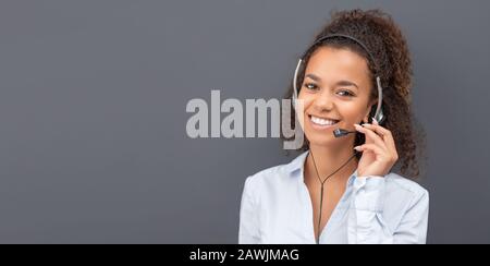 Employé du centre d'appels isolé sur un fond gris. Un opérateur souriant au travail. Jeune employé travaillant avec un casque. Banque D'Images