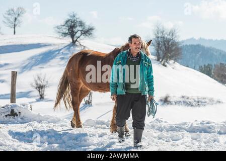 Village de Grachevo, Rhodopes, Bulgarie - 8 février 2020: Vieil homme avec son cheval dans la rue dans le village de Grachevo, haut en montagne d'hiver. Banque D'Images