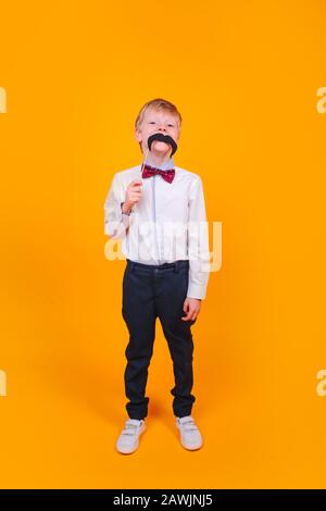 un petit enfant qui plaisante avec une moustache sur fond jaune Banque D'Images