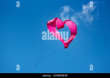 Un cerf-volant en forme de coeur rose volant dans l'air sur un fond bleu clair ciel Banque D'Images