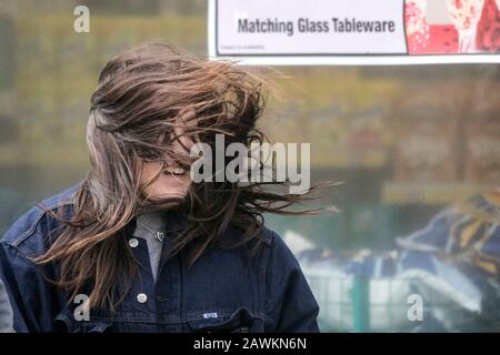 Une jeune fille ayant un mauvais jour de cheveux comme ses cheveux soufflant dans le temps du vent provoquant des hangles comme les vents de force de gale balaient dans les rues Banque D'Images