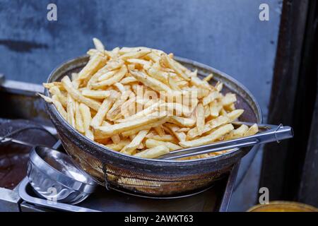 Vue sur les frites maison et fraîchement frites/cuites dans un bol en métal avec du tong alimentaire. Délicieux en-cas, croustillant et croustillant. Banque D'Images