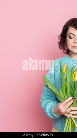 Belle vieille femme avec maquillage professionnel fumé et tenue de coiffure fleurs de tulipes sur fond rose Banque D'Images