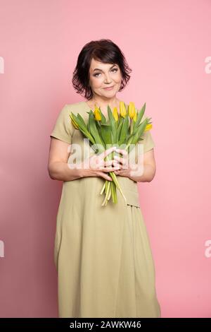 Belle vieille femme avec maquillage professionnel fumé et tenue de coiffure fleurs de tulipes sur fond rose Banque D'Images