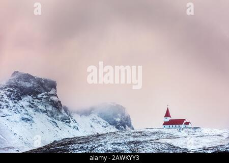 Vik i Myrdal église, à Vik, Islande, contre fond enneigé de montagne et ciel rose au crépuscule. Cette église picturequese à toit rouge est perchée sur un salut Banque D'Images